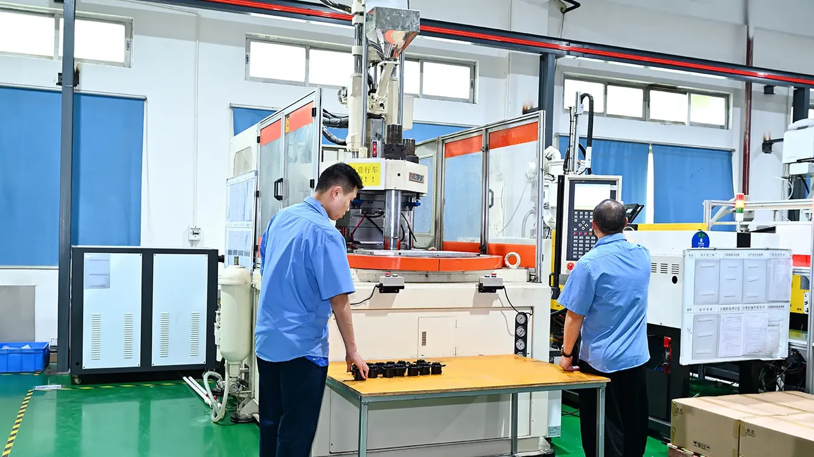 Operator at a vertical injection molding cell arranging rows of small black molded button parts