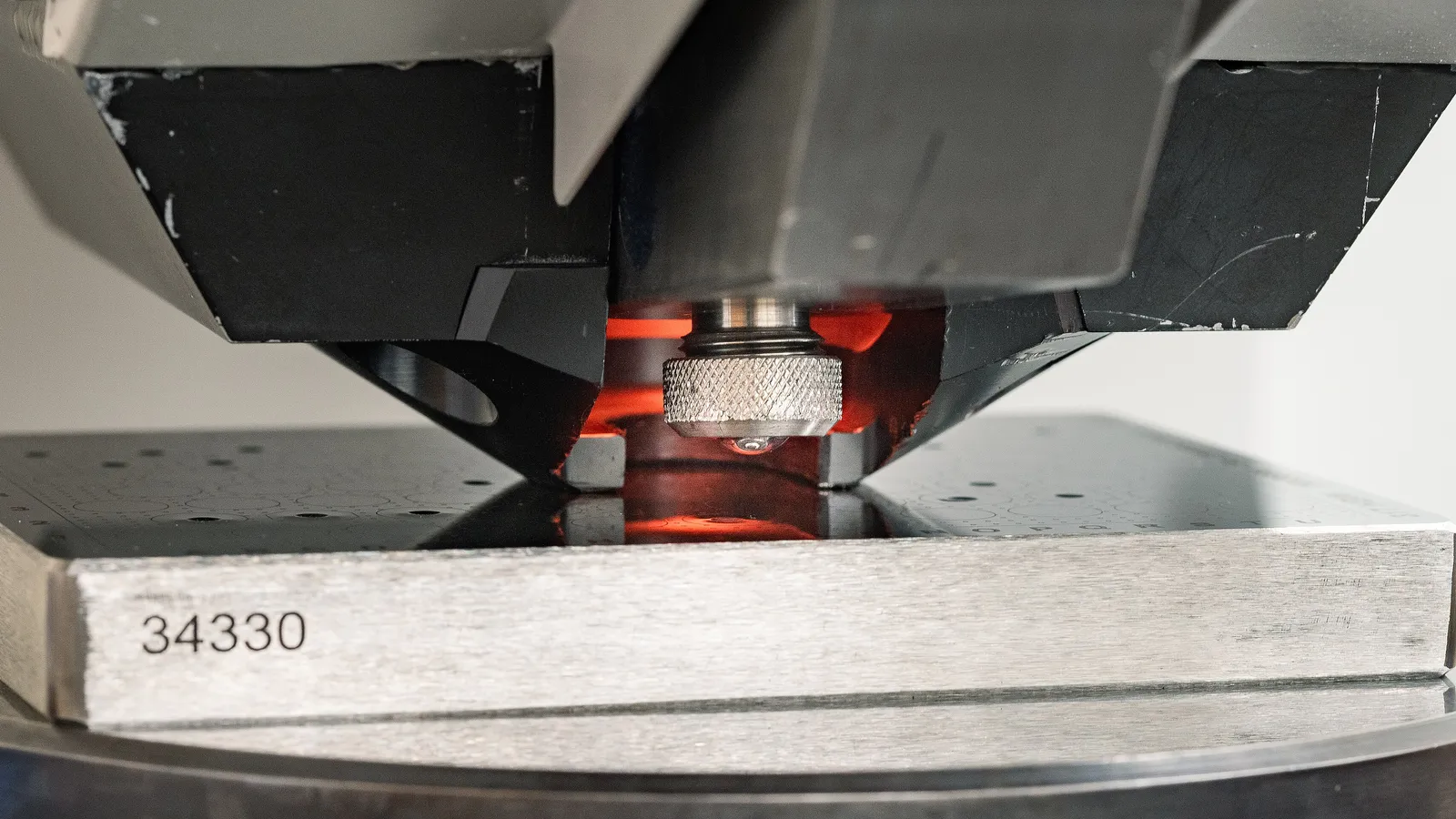 Brinell hardness tester ball indenter descending onto a specimen plate marked with a grid of test indentations