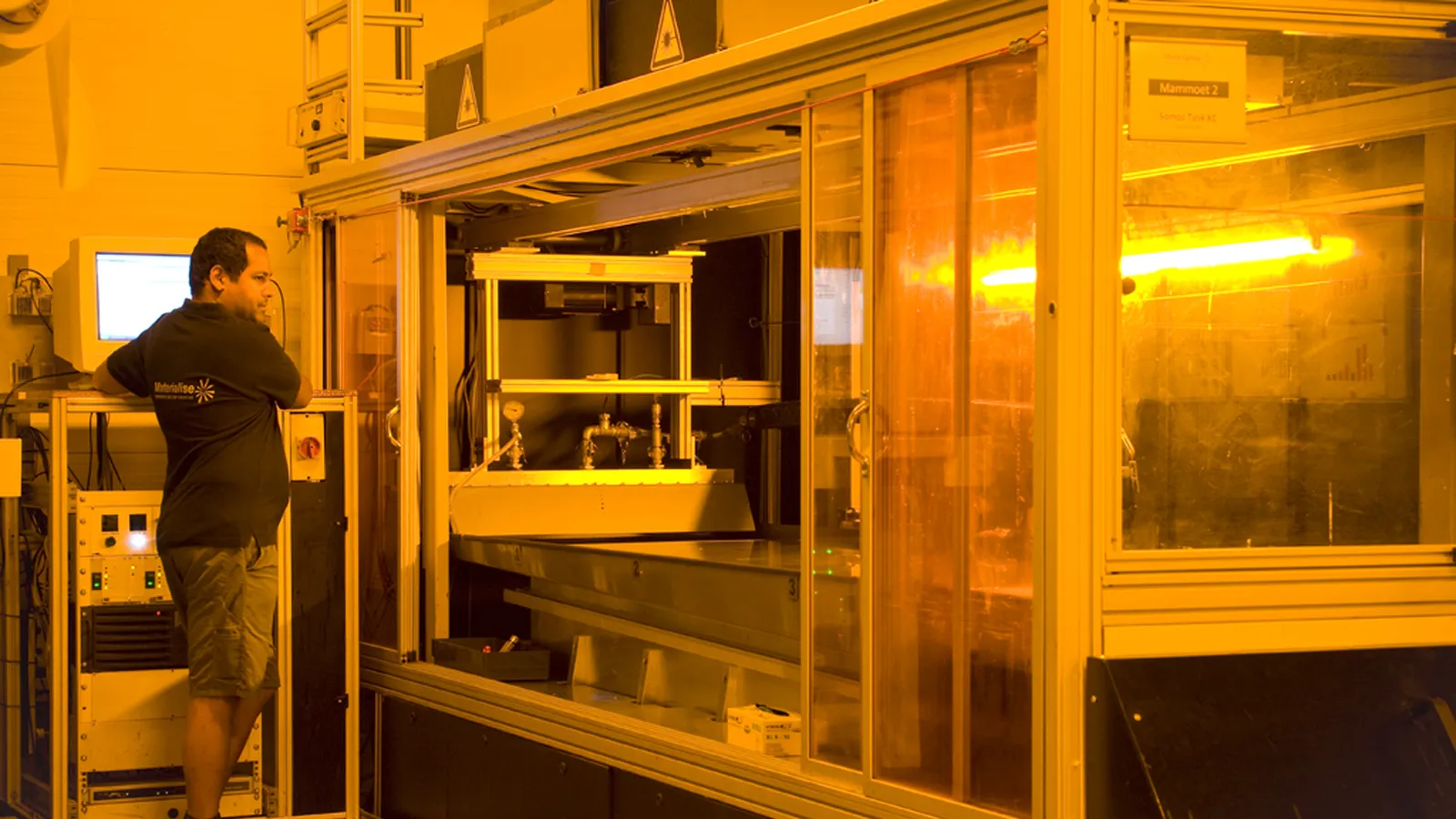 Operator at a large amber-lit industrial 3D printer